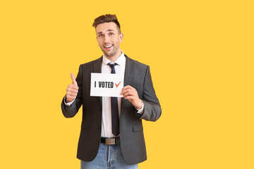 Businessman holding paper with text I VOTED and showing thumb-up on color background