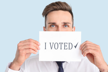 Businessman holding paper with text I VOTED on color background