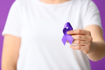 Woman with purple ribbon as symbol of World Cancer Day on color background, closeup