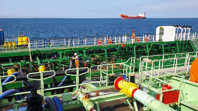ship workers in uniform set bunkering hoses against nice blue sea with distant red tanker waiting on raid on sunny day