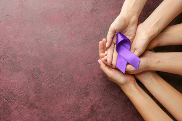 Female hands with purple ribbon as symbol of World Cancer Day on color background