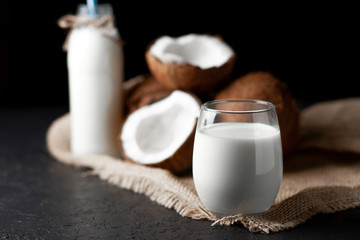 fresh coconut milk in a glass against a dark background, cosmetic cream from coconut on a cloth