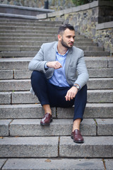 Portrait of a bearded man near the big steps of an old European castle. Businessman thinking over a future project. Fashionable guy with stylish clothes.