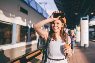 Tourism and travel in the summer. Vacations for the student. Work and travel. Caucasian young woman drinks coffee on the platform of the railway station against the background of the train - Powered by Adobe