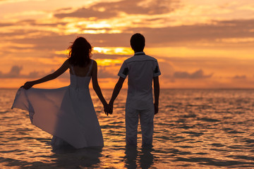 Beautiful wedding photoshoot of a couple. Beautiful bride in white wedding dress and groom having fun on shore sea. Tropical sea in the background. Summer vacation concept. Sunset on the ocean