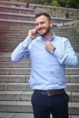 Portrait of a bearded man near the big steps of an old European castle. Businessman talking on the phone. Fashionable guy with stylish clothes.