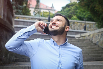 Portrait of a bearded man near the big steps of an old European castle. Businessman talking on the phone. Fashionable guy with stylish clothes.