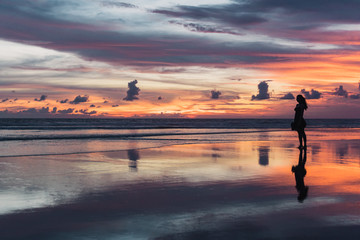 Fototapeta na wymiar BALI, Indonésia: por do sol na praia de Seminyak e silhueta de mulher. Céu colorido..