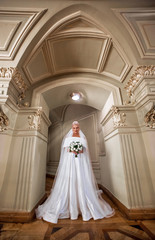Obraz na płótnie Canvas Luxury blonde bride with a white bouquet stands under the arch