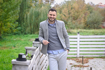 Portrait of a sexy man dressed in a suit. Fashionable guy in the autumn nature near a white wooden fence. Businessman relaxes. Skok photo for design © snb2087