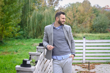 Portrait of a sexy man dressed in a suit. Fashionable guy in the autumn nature near a white wooden fence. Businessman relaxes. Skok photo for design © snb2087