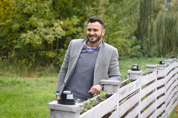 Portrait of a sexy man dressed in a suit. Fashionable guy in the autumn nature near a white wooden fence. Businessman relaxes. Skok photo for design © snb2087