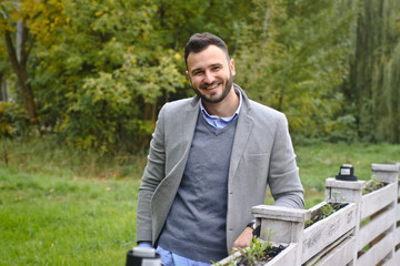 Portrait of a sexy man dressed in a suit. Fashionable guy in the autumn nature near a white wooden fence. Businessman relaxes. Skok photo for design © snb2087