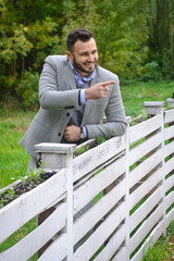 Portrait of a sexy man dressed in a suit. Fashionable guy in the autumn nature near a white wooden fence. Businessman relaxes. Skok photo for design © snb2087