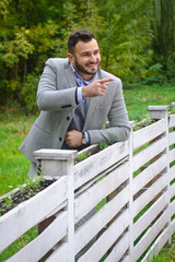 Portrait of a sexy man dressed in a suit. Fashionable guy in the autumn nature near a white wooden fence. Businessman relaxes. Skok photo for design © snb2087