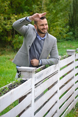 Portrait of a sexy man dressed in a suit. Fashionable guy in the autumn nature near a white wooden fence. Businessman relaxes. Skok photo for design © snb2087