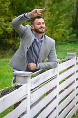 Portrait of a sexy man dressed in a suit. Fashionable guy in the autumn nature near a white wooden fence. Businessman relaxes. Skok photo for design © snb2087