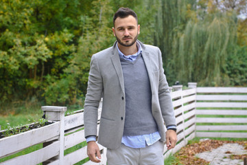Portrait of a sexy man dressed in a suit. Fashionable guy in the autumn nature near a white wooden fence. Businessman relaxes. Skok photo for design © snb2087