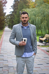 Obraz premium Young sexy guy strolling through the autumn, summer park. man drinking coffee, tea in the nature. European countryside. Stock Photo for design