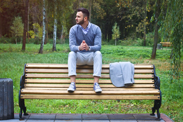 Young sexy guy sitting on a bench in an autumnal, summer park. A man contemplating new ideas while walking. European countryside. Stock Photo