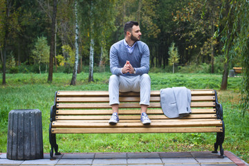 Young sexy guy sitting on a bench in an autumnal, summer park. A man contemplating new ideas while walking. European countryside. Stock Photo