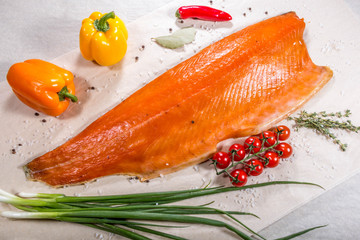 Smoked fish next to vegetables: tomatoes, onions, colored peppers and garlic. Still life