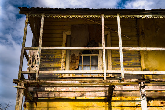 Old abandoned yellow two storey/ story wooden home structure in rural countryside. Deserted dwelling damaged and unsafe for living. Haunted mansion property.
