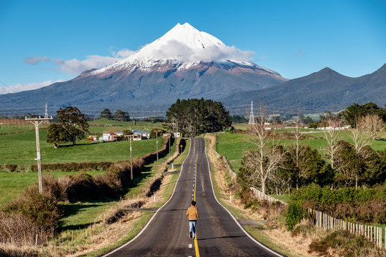 Man runs on a straight road toward snow mountain. Running outdoors concept. Achieve goal, motivation and determination concept.
