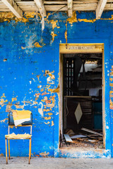 Open doorway abandoned vintage brick wall Police Canteen building with stripping blue surface paint on facade, no door and rubble/ junk inside. Forgotten old property with walls cracked falling apart.