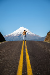 Man standing on top of road overlooking top of mount taranki peak in New Zealand. Success destination goal achievement concept background.