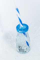 My bottle water bottle with a blue cap and blue straws with splashes of water on a light background