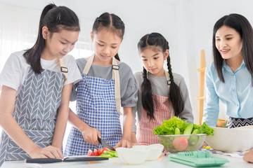 Asian female and asian children cooking organic salad, they use knife cut fresh tomato on chopping board, asian children  learning to cook in kitchen room
