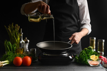 Chef pouring oil on a frying pan, freezing in motion. On a background with ingredients. Homemade...