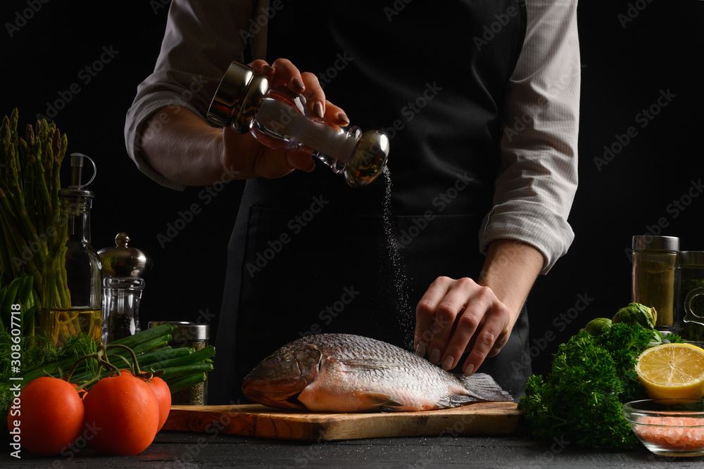 Wall mural chef cooks fresh fish on the background with ingredients, salts it before cooking, freezing in motio