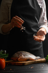Seafood, Chef cooks fish, salt with sea salt, freeze in motion. On a black background with ingredients on the table. Healthy and healthy food, sale of seafood, fish shops, vertical frame.