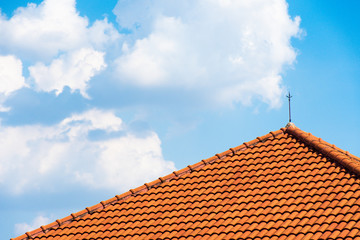 The orange brick roof with lightning poles on the top of the roof and a background in the sky and clouds.