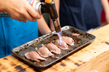 A close-up view of a chef using a burnt beef on top of sushi rice in an iron tray.