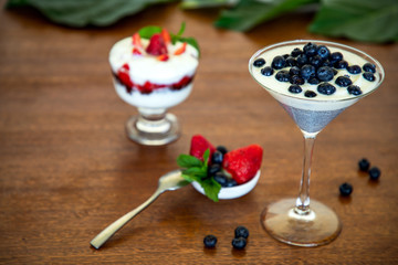 Yogurt with blueberries, strawberries, chia seeds and mint on a wooden table, blurred background with leaves