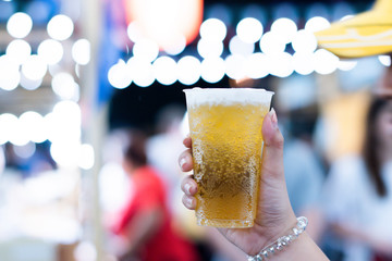 A close up shot of the hand holding a glass of butter beer and blurred background.