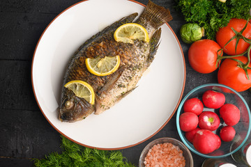 Cooked fish with lemon, on a black wooden background, with ingredients and vegetables. Delicious and healthy food.