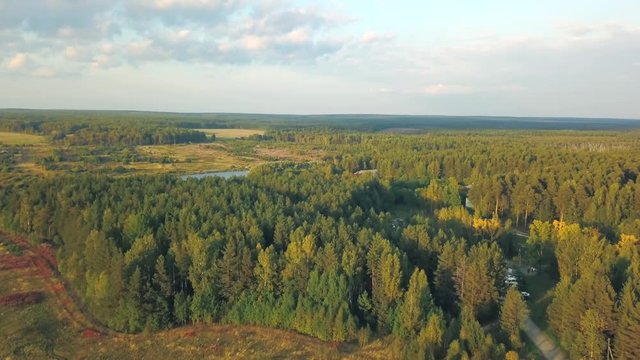 Aerial view of large green fields, forests and road at the sunset against blue cloudy sky in summer or in the beggining of the autumn. Stock footage. Beautiful countryside views