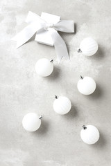 White Christmas Tree Ornaments on a light gray table top with a white gift box and bow.