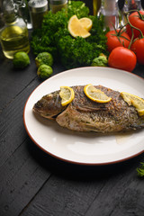 Tasty fish cooked with lemons on a background of fresh vegetables.Vertical frame