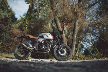 Fototapeta na wymiar Cafe racer scrambler motorcycle, old fashioned vehicle with modern materials on forest background