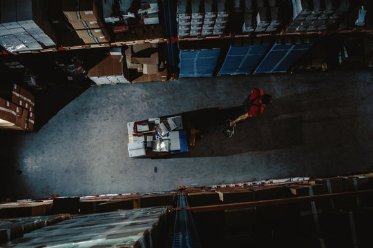 Strong Worker On Big Warehouse. Lot Of Boxes At Dark Interior And Top Aerial View