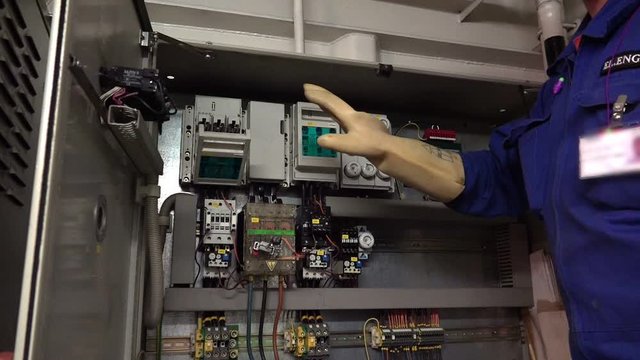 electrical engineer in uniform and protection gloves checks appliances and sensor probes in tanker engine control room