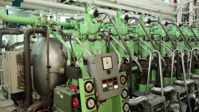 main engine unit with cylinder heads and light green control panel works in tanker propulsion compartment low angle shot