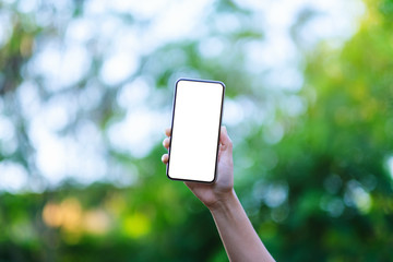 Mockup image of a hand holding black mobile phone with blank desktop screen with green nature background