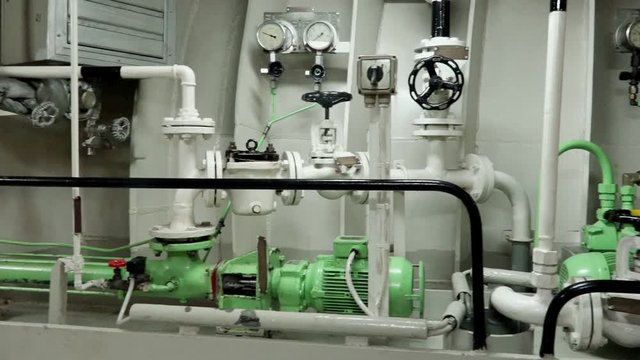 multiple closed conduits with curved pipes and green pumps stretch along engine room in Onyx tanker close motion