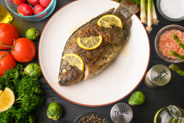 Eastern or European cuisine, Fried fish with fresh vegetables, on a wooden black background. I also eat healthy food. Seafood, recipe book, selling fish, restaurant business